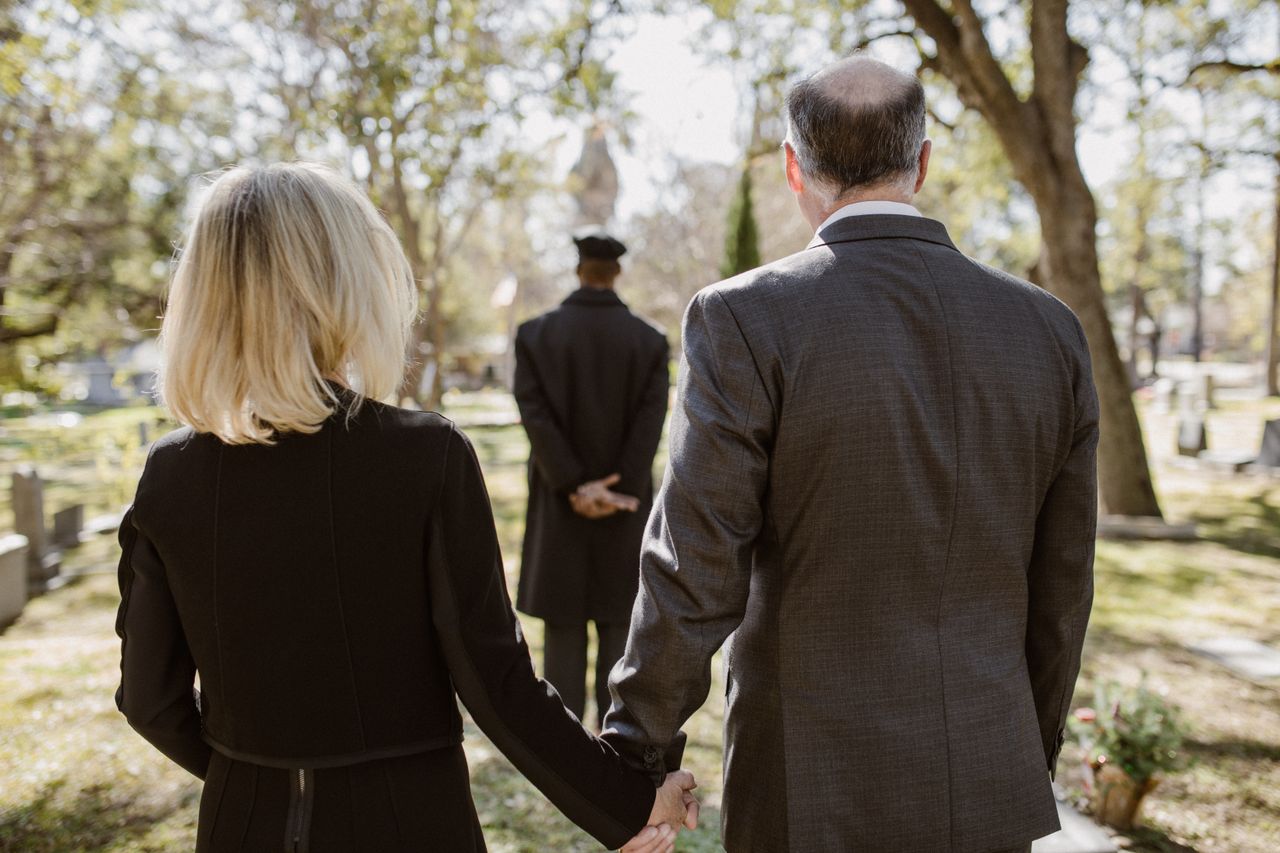 Home A couple holds hands in a cemetery during a memorial service, symbolizing love and remembrance.