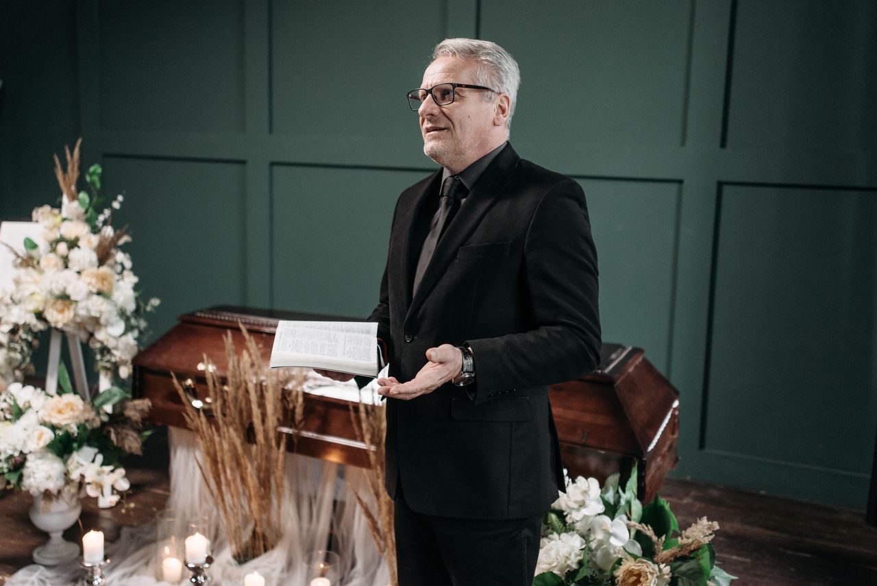 Pastor conducting a solemn funeral service with coffin and floral arrangements.