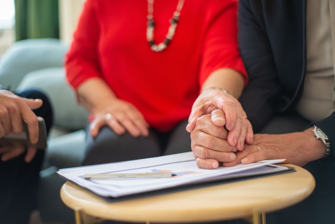 Home Senior couple holding hands over a table with documents, symbolizing support in an office setting.