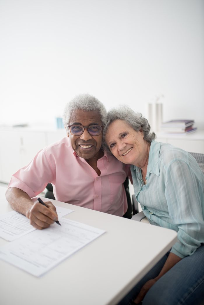 Home Happy elderly couple sitting at a desk, smiling and signing documents. Perfect for insurance and lifestyle themes.